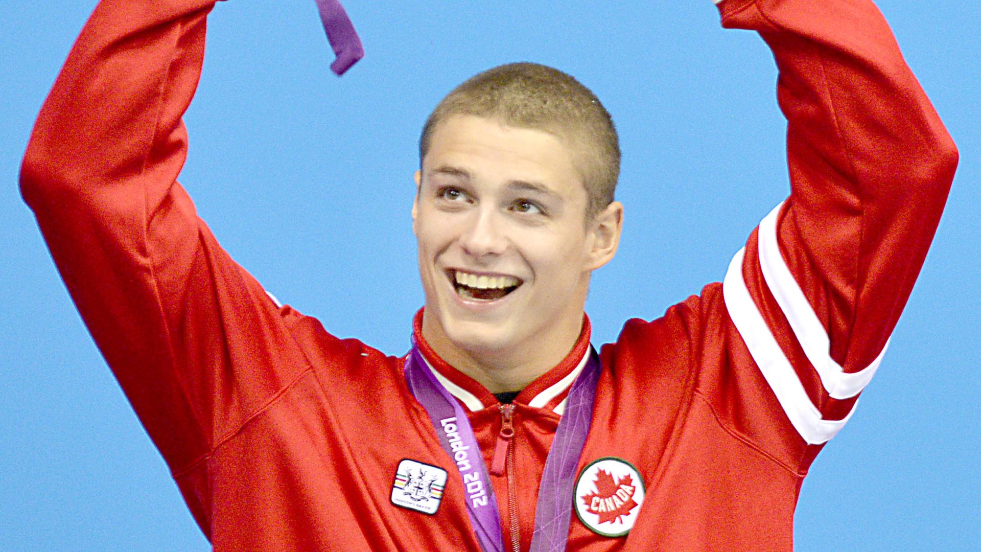 Nathan Stein raises his hands in celebration, wearing a gold medal and holding a bouquet.